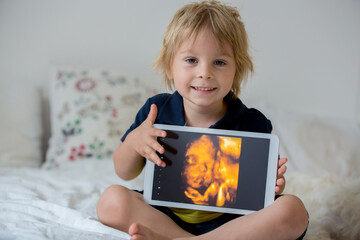 Cute toddler child, holding a picture of his little unborn baby sister