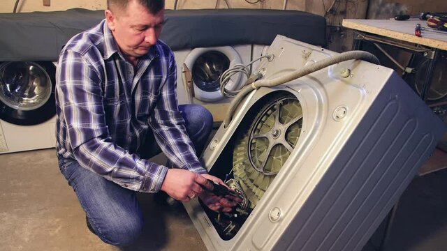 The foreman removes the parts from the washing machine. The man disassembles, assembles, repairs the washing machine. Business concept in the field of maintenance and repair services. UHD 4K.