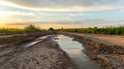 Rural road with a puddle at sunset