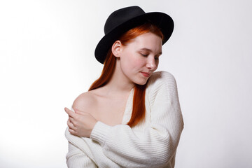 A sensual portrait of a young attractive woman with red hair and a black hat on a white background.