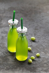 Fresh gooseberry juice in a glass bottle with a lid and a straw on a dark gray background