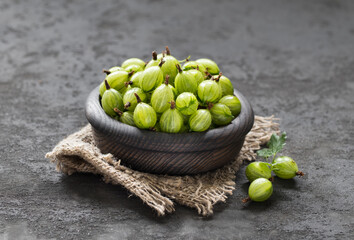 Fresh gooseberries in a wooden bowl on a linen napkin on a dark gray background