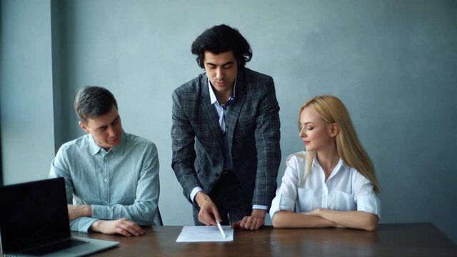 Front view of financial advisor attorney explaining contractual details to happy couple in modern office room. Portrait of male lawyer talking with young married couple during meeting in law office.