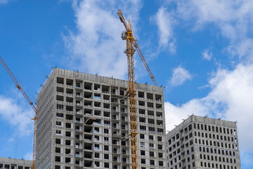 Fototapeta na wymiar Construction cranes and unfinished residential buildings against clear blue sky. Housing construction, apartment block with scaffolding