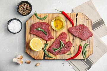 Fresh raw meat steaks and spices on light grey table, flat lay