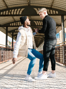 Joyful young multiethnic guys giving dap on pedestrian bridge