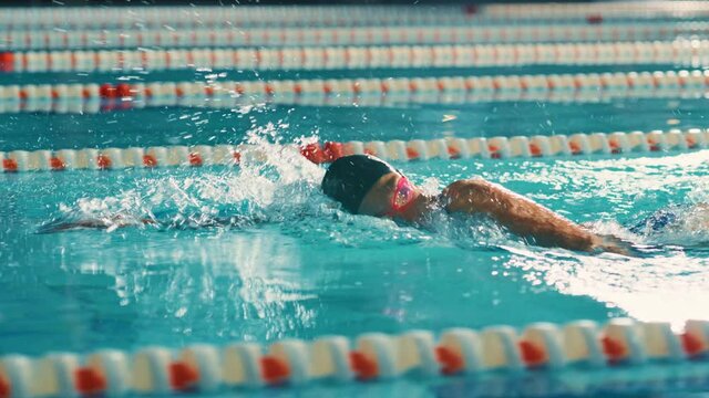 Successful Female Swimmer Racing in Swimming Pool. Professional Athlete Determined to Win Championship using Freestyle. Colorful Cinematic Shot. Side View Cinematic Tracking Shot