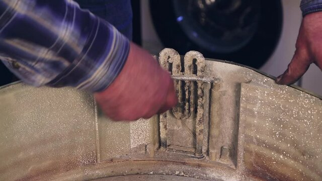 The hands of the master clean the heating element from plaque. The man disassembles, assembles, repairs the washing machine. Business concept in the field of maintenance and repair services. UHD 4K.