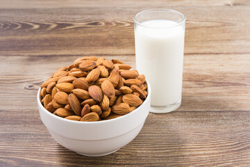 Almond nuts in a white bowl and milk in glass on wood background. selective focus.front view.
