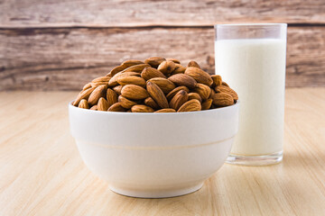 Almond nuts in a white bowl and milk in glass on wood background. selective focus.front view.