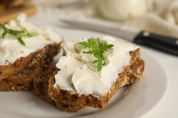 Bread with cream cheese and arugula on plate, closeup