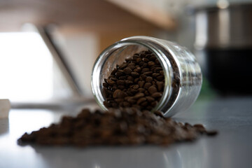 Bocal rempli de grains de café, renversé sur le plan de travail d'une cuisine. Tas de grains de café devant le bocal.