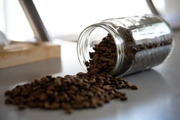 Tuinposter Bocal rempli de grains de café, renversé sur le plan de travail d'une cuisine. Vue de trois quart. © Morgane