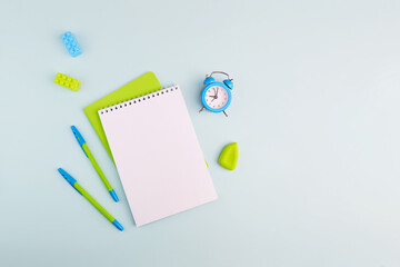 School supplies on light blue background. Notebook, pens, alarm clock and rubber bands. Flat lay, copy space. Back to school. 