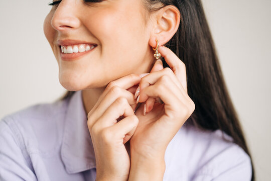 Crop smiling woman touching earring on light background