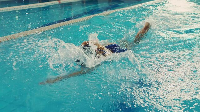 Beautiful Female Swimmer Using Front Crawl, Freestyle in Swimming Pool. Professional Athlete Determined to Win Championship. Cinematic Slow Motion, Stylish Colors, Artistic Tracking Shot