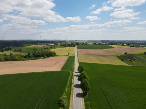 Aerial view of road between fields in the countryside with nice blue cloudy sky 
