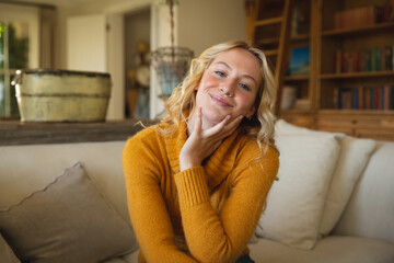 Obraz premium Portrait of happy caucasian woman sitting on couch in luxury living room, leaning on hand, smiling