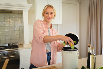Portrait of smiling caucasian woman standing in kitchen preparing food, composting vegetable waste