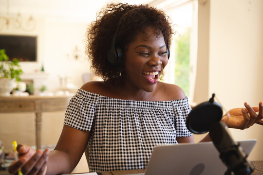 Happy african american woman wearing headphones and using microphone, singing during podcast