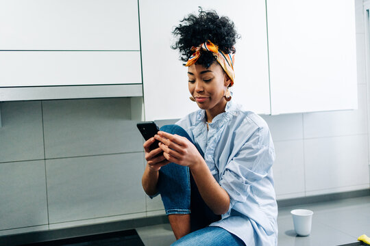 Black woman browsing smartphone in kitchen