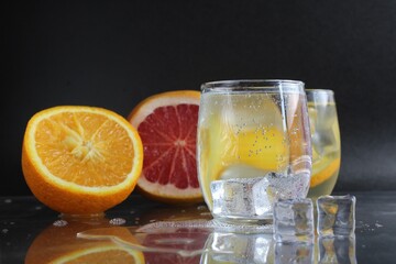 Cooking Lemonade Water in a glass of ice and fruit orange grapefruit on a black background. Summer drinks. A lemonade drink