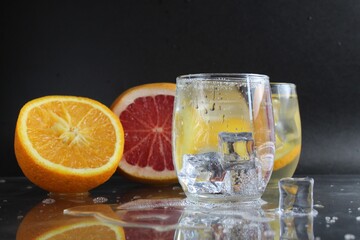 Cooking Lemonade Water in a glass of ice and fruit orange grapefruit on a black background. Summer drinks. A lemonade drink