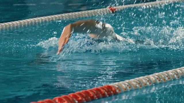 Successful Male Swimmer Racing in Swimming Pool. Professional Athlete Determined to Win Championship using Front Crawl Freestyle. Colorful Cinematic Shot. Front View Portrait Slow Motion
