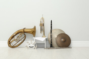 Different percussion and wind musical instruments near white wall indoors