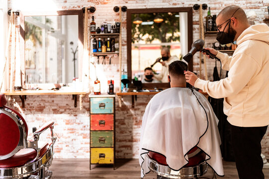 Barber with client using hair dryer in salon