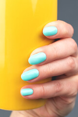 Female hand with beautiful manicure - turquoise, mint blue nails with bright yellow cup against gray background, closeup. Nail care concept