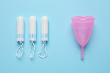 Menstrual cup and tampons on light blue background, flat lay