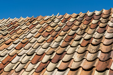 close up view of red and orange burned clay roof tiles undeer a clear blue sky