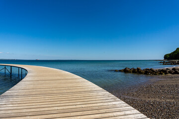 curved wooden boardwalk leads out into the blue ocean