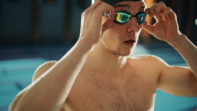 Handsome Professional Male Swimmer in Swimming Pool, Wearing Cap and Glasses, Looks Confidently at the Camera, Ready to Win the Championship. Cinematic Portrait of Confident Man. Tilt Dutch Angle