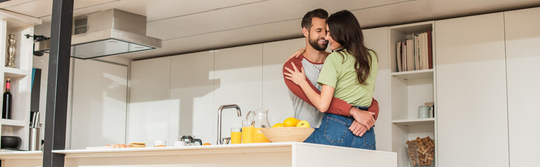 Obraz na płótnie Canvas Positive couple hugging near breakfast and orange juice, banner