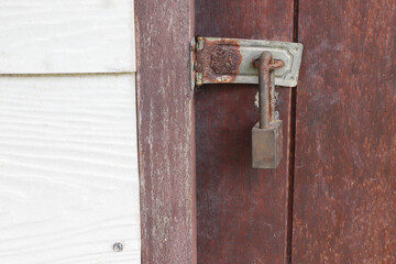 Old and rusty padlock locked at the wooden door closeup.