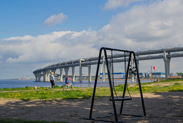 
provincial village is swayed by the wind against the background of large round highway bridge in the blue sea and sky with clouds. People, leisure, concept past and future building world