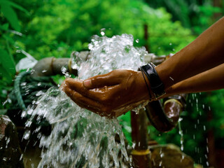 Boy hand collecting water on tap at green natural blur background.