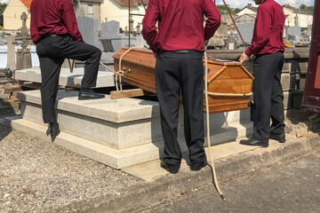 Porters lower the coffin into the grave - obrazy, fototapety, plakaty