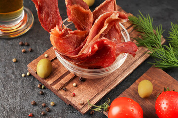 Natural snack for beer. Pieces of spicy jerky meat in a glass cup on a dark background. Condiments...
