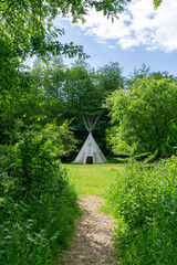 gravel hiking path leads up to a large teepee in the forest