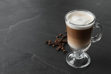 Glass cup of delicious layered coffee and beans on black table, space for text