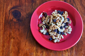 red plate with mixed nuts dried fruits on wooden background from above. Healthy food and snack. Walnut, pistachios, almonds, hazelnuts and cashews. horizontal copy space