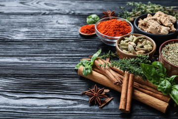Different natural spices and herbs on black wooden table. Space for text