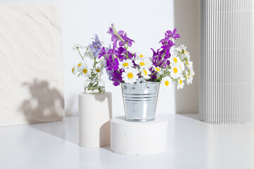 Still life of wildflowers and daisies in a decorative bucket on pedestals