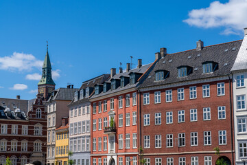 colorful historic cityscape and buildings with a church spire in the background under a blue sky with white cumulus clouds