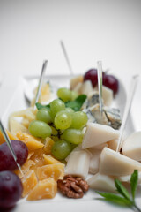 closeup of cheese plate with grape, walnuts and honey on white background