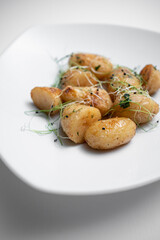 closeup of tasty roasted potatoes with microgreen on plate on white background