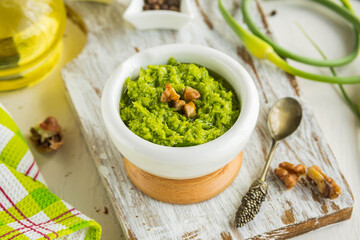 Garlic arrow pesto sauce with walnuts in a white mortar on a light concrete background. Sauce recipes.